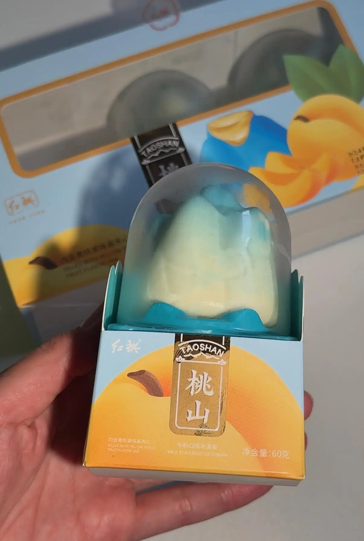 Blue mountain propitious fruit ice cream in transparent dome packaging held above yellow and blue box from RD International Market
