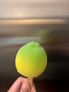 Hand holding a yellow and green frozen popsicle against a blurred background